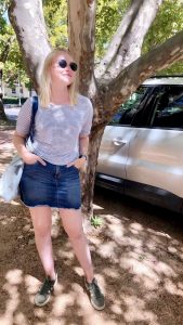 blonde girl wearing skirt and top in front of tree at university